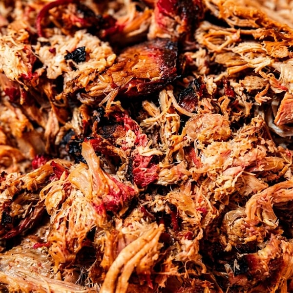 Close-up of a large pile of freshly pulled pork, showing its tender, smoky texture.