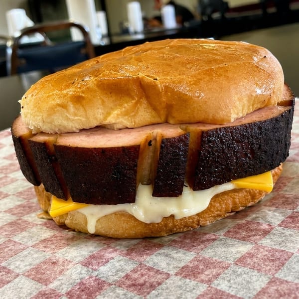 A thick, grilled bologna sandwich with melted cheese on a bun, on checkered paper.